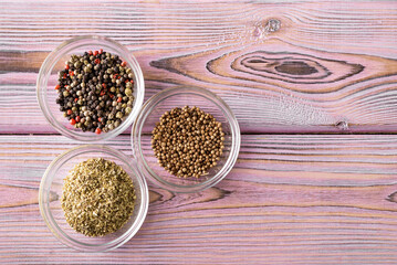 Various spices in glass bowls on a purple wooden background. Black and red pepper, oregano, coriander.