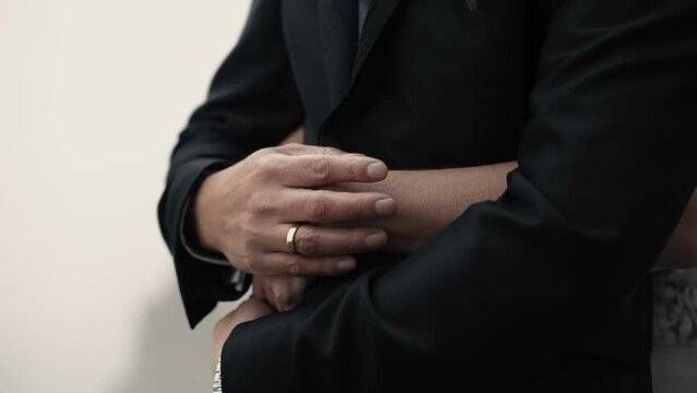Grooms hand with a golden ring stroking brides hand gently while bride is hugging him from behind