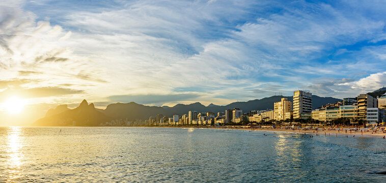 Panoramic image of Ipanema beach during sunset with the sea, mountains and city buildings