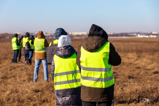 Group of many people watching planes landing and take off airport runway field planespotting conference warm morning time. Planespotters in safety vest waiting aicraft arrival approaching departure