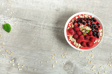 Smoothie with raspberries, black currants and oatmeal in a white cup on a gray wooden table. High angle view, selective focus with copy space