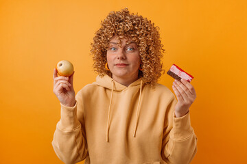Attractive 30s woman made wrong choice between cake and fresh apple isolated over yellow. Dieting...