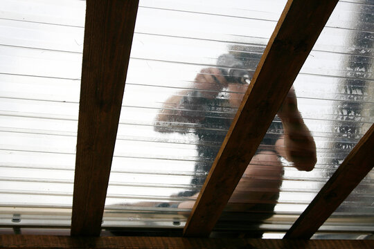 Man working using power tool to attach clear PVC roofing sheets on home terrace outdoors.