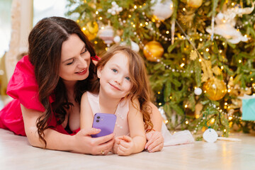 mother and daughter under the Christmas tree with a smartphone.