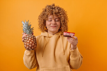 Cheerful young happy woman made wrong choice between cake and fresh pineapple isolated over yellow.