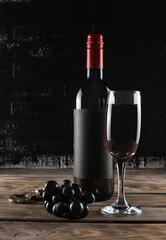Fototapeta na wymiar Bottle and glass of red wine on a wooden table. Black grapes and corkscrew in the background