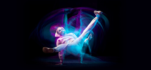 One energy young flexible sportive man dancing hip-hop or breakdance in white outfit on dark background in mixed blue neon light. Sport, art, action, moves
