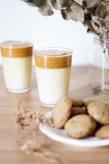 Dalgona coffee with milk, dried eucalyptus vase and cookies on wooden table.
