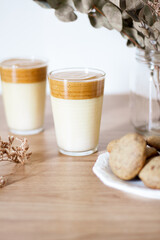 Dalgona coffee with milk, dried eucalyptus vase and cookies on wooden table.