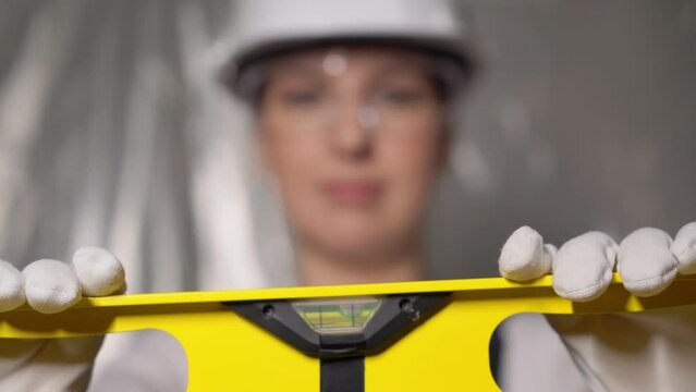 Woman builder in blue overalls and white hard hat helmet with level.
