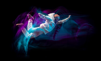 One energy young flexible sportive man dancing hip-hop or breakdance in white outfit on dark...