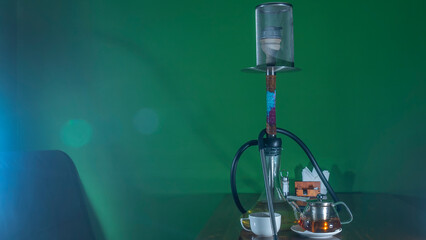 Traditional Arabian shisha and tea with lens flare. A pot of tea and Smoking hookah on a dark green background.