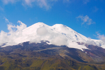 A double-headed snowy mountain peak against a background of blue sky and swirling clouds
