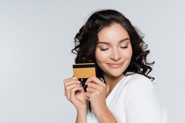 pleased young woman holding credit card isolated on grey.