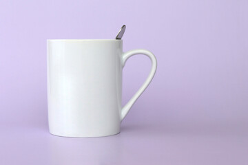 A large white mug with coffee and a spoon inside on a purple background, space for copying