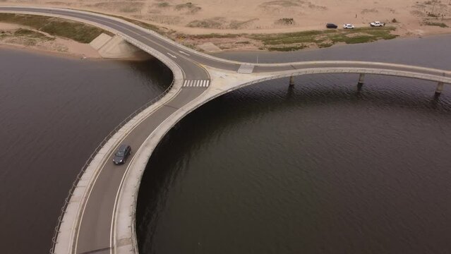 A drone follows a car on a circular bridge at Laguna Garzon