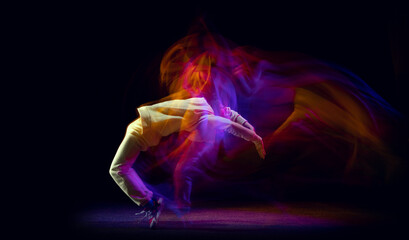 Solo dance. Young flexible sportive man dancing hip-hop or breakdance in white outfit on dark background in mixed yellow neon light. Beauty, sport, youth, action, moves