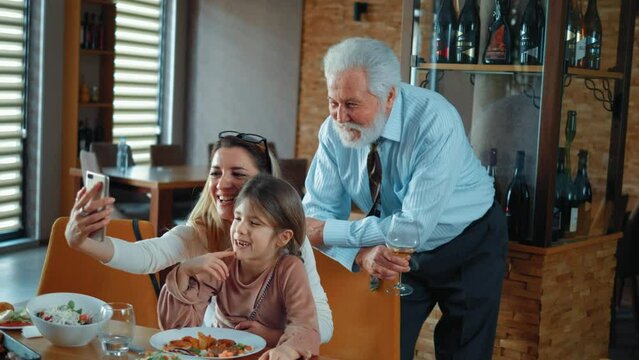 Three-generation family granddaughter young mother and old grandfather taking a selfie photo at the family lunch