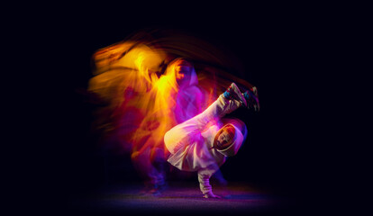Solo dance. Young flexible sportive man dancing hip-hop or breakdance in white outfit on dark...