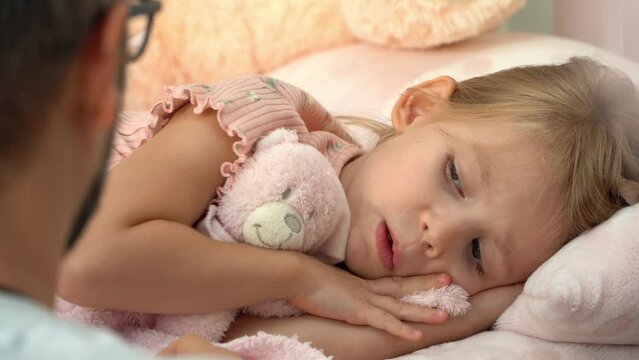 Father touches forehead of sick little girl and measure temperature with thermometer. Child lies in bed with fever and coughs. Treatment for illness, flu and cold