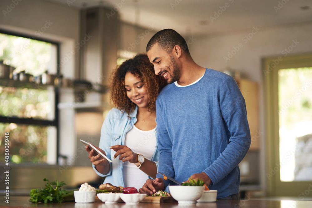 Poster Using a step by step online recipe. Shot of a happy young couple using a digital tablet while preparing a healthy meal together at home.