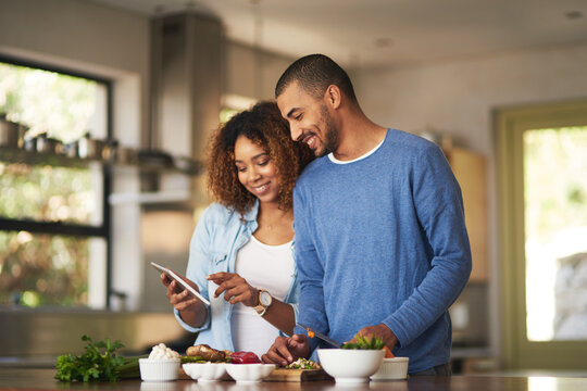 Using a step by step online recipe. Shot of a happy young couple using a digital tablet while preparing a healthy meal together at home.