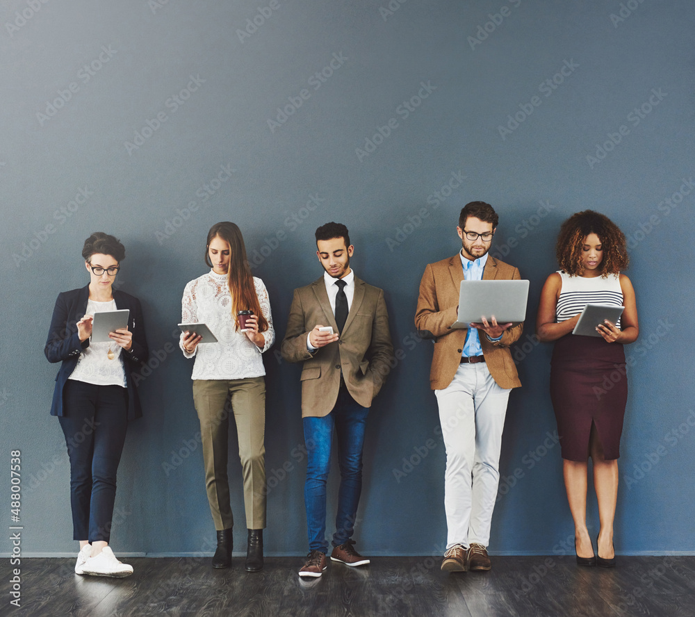 Poster Waiting it out in the name of success. Studio shot of a group of businesspeople using wireless technology while waiting in line against a gray background.