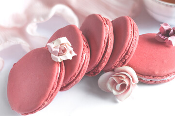 Festive raspberry macaroons, close-up side view with flowers on pink fabric. Blurred background with selective focus
