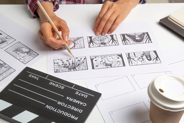 The artist draws sketches of the storyboard of the characters of the scenes for the film or cartoon with a movie clapperboard on the desktop.