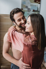 Naklejka premium happy young woman in pink silk robe hugging cheerful man.