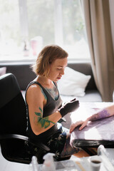Tattoo parlor, pretty European red-haired girl makes a tattoo on arm. Woman creates a tattoo on a female hand by a professional tattoo artist