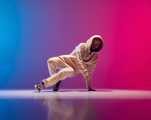 Studio shot of young flexible sportive man dancing breakdance in white outfit on gradient pink blue background. Concept of action, art, beauty, sport, youth