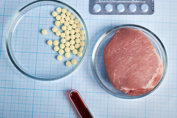 GMO meat in a Petri Dish and pharmacy capsules - photo on a graph paper. Artificial meat in flat...