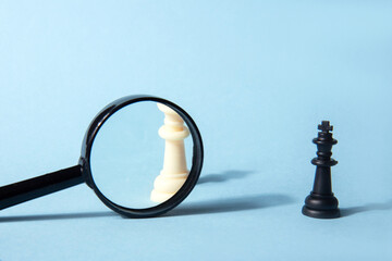 White chess queen, black chess queen and magnifying glass on a blue background. Abstract...