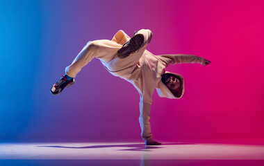Studio shot of young flexible sportive man dancing breakdance in white outfit on gradient pink blue...