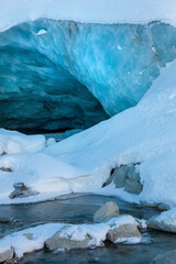 Entrée d'une caverne glaciaire au glacier de Zinal dans les Alpes suisses et la rivière qui en sort.