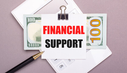 On a gray background, a white calculator, a pen, banknotes and a sheet of paper under a black paper clip with the text FINANCIAL SUPPORT. Business concept
