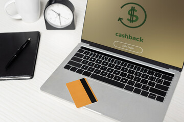 credit card on laptop with cashback on screen near notebook and cup on white desk.