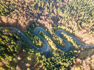 Winding road from high mountain pass, in summer time. Aerial view of a green forest and an empty road traffic