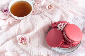 Composition of delicious french macaroons with a cup of tea. On a pink fabric decorated with flowers. Overhead view, selective focus in daylight