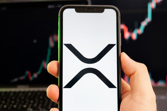 XRP cryptocurrency logo on the screen of a smartphone in mans hand with a growing trend on the chart on a green background.