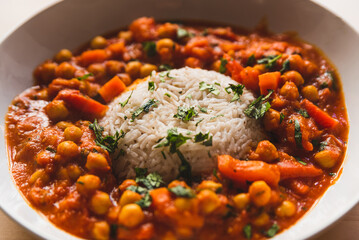 vegan chickpeas curry. close up of fresh vegetarian indian curry known as chana masala with basmati rice and coriander leaves on table with soft natural light