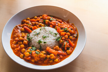 vegan chickpeas curry. close up of fresh vegetarian indian curry known as chana masala with basmati rice and coriander leaves on table with soft natural light