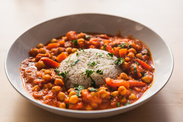 vegan chickpeas curry. close up of fresh vegetarian indian curry known as chana masala with basmati rice and coriander leaves on table with soft natural light