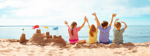 Four happy children sitting onthe sea coast and raising up their hands. - 488019385