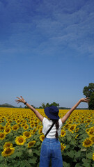 Asian woman standing and open arms in the sunflower field on sunny day