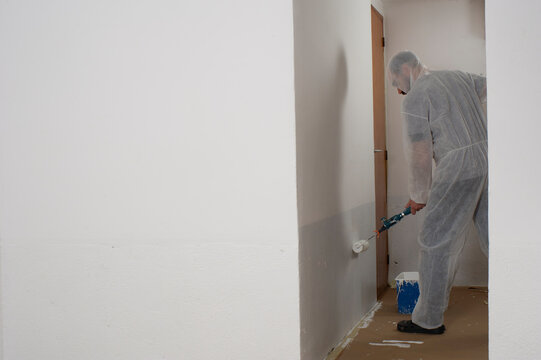 Hombre pintando pared blanca, delante pared blanca con gran superficie para incluir textos 