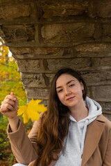 Dark haired young white woman holding a yellow maple leaf in autumn park