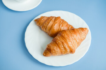 2 large croissants on a white plate, on a blue background. Morning breakfast in France. Fresh Baking with your own hands.