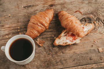 cut croissant with butter and strawberry jam with a cup of coffee, on a wooden background, top view.